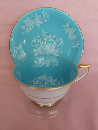 A beautiful Aynsley cup and saucer having stark white roses and florals overtop a sky blue backgroun...