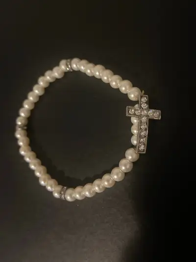 This is a beautiful pearl bracelet featuring faux pearls and a cross charm, perfect for adding a tou...
