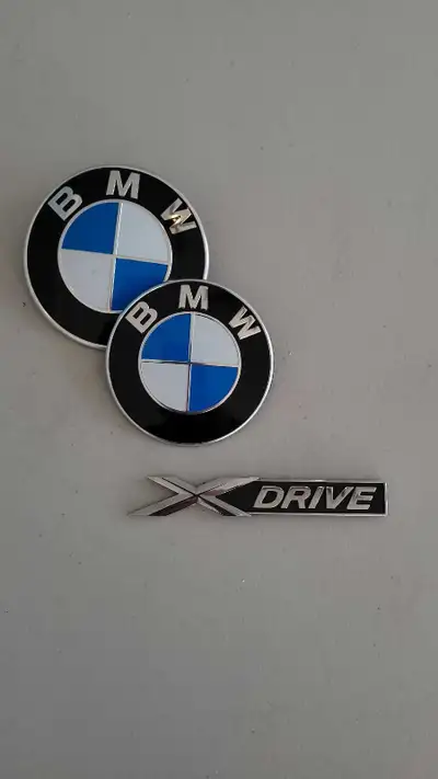2 logos BMW (emblèmes capot/coffre) en parfait état, finition noire et chrome avec le bleu/blanc cla...