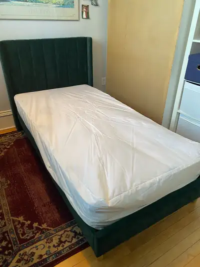Twin mattress frame dark green fabric and mattress. Mattress has a protective cover and a mattress c...