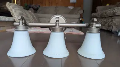This bathroom vanity light fixture features three frosted glass shades and a bronze finish, adding a...
