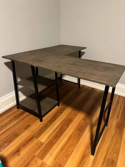 This L-shaped desk features a dark wood-look finish with a black metal frame. It has two open shelve...