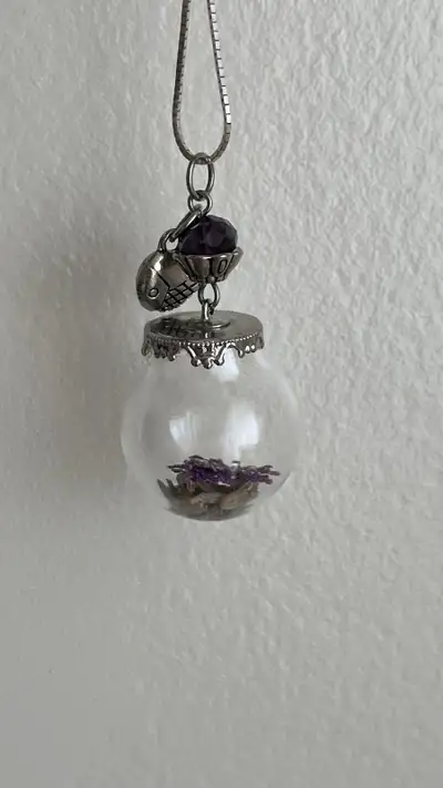 Silver tone pendant. Features a small glass globe filled with dried purple flowers. A small silver b...