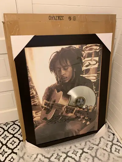 This is a framed art piece featuring Bob Marley with a silver record accent; it is in new condition....