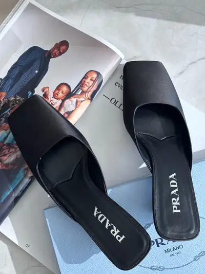 Prada 'Calzature Donna Mule' in black satin with a square toe and triangular toe. Featuring a Prada...