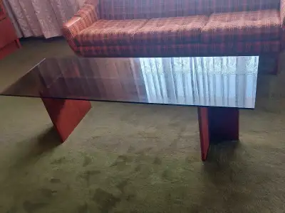 This vintage coffee table features a sleek glass top and unique trapezoid-shaped wood legs, making i...