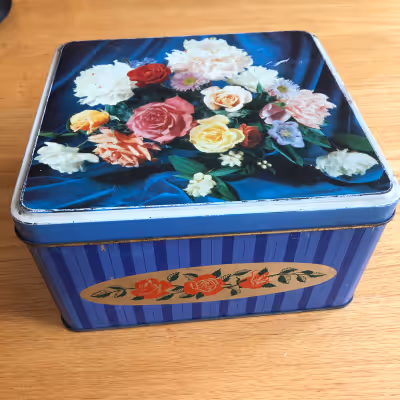 Almost square biscuit tin, decorated with a photo of a floral arrangement. Inside of lid reads "A Pr...
