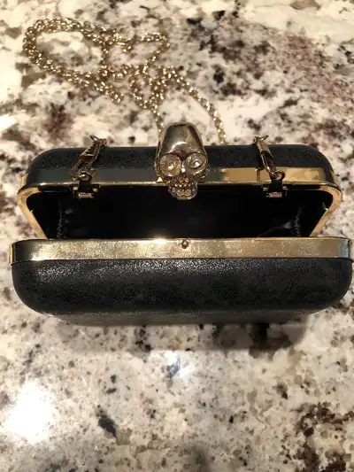 Gold skull with rhinestone eyes acts as a latch on black leather purse. 50” gold chain can be used w...