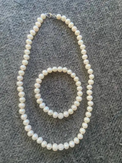 This is a used pearl necklace and bracelet set featuring lustrous, classic pearls. The necklace is a...