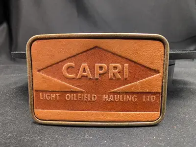 This vintage brass and leather belt buckle features the logo for Capri Light Oilfield Hauling Ltd. L...