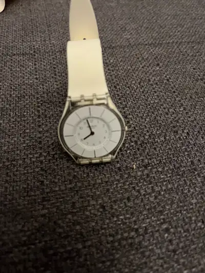 This Swatch watch features a sleek, minimalist design with a white band and a subtle face, perfect f...