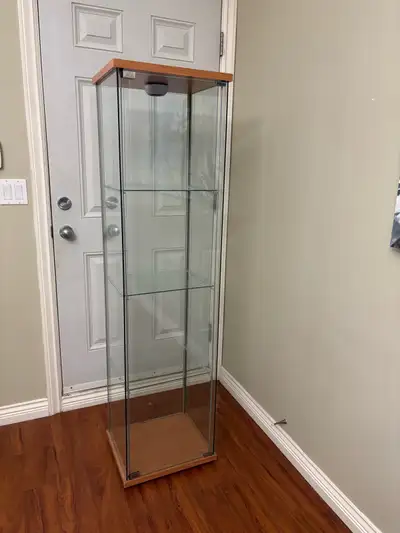 Showcase your prized possessions in this elegant glass display cabinet, featuring a light wood frame...
