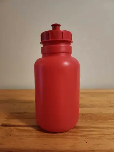 Red plastic water bottle. Features a screw-on cap with a flip-top spout. Good for hydration on the g...