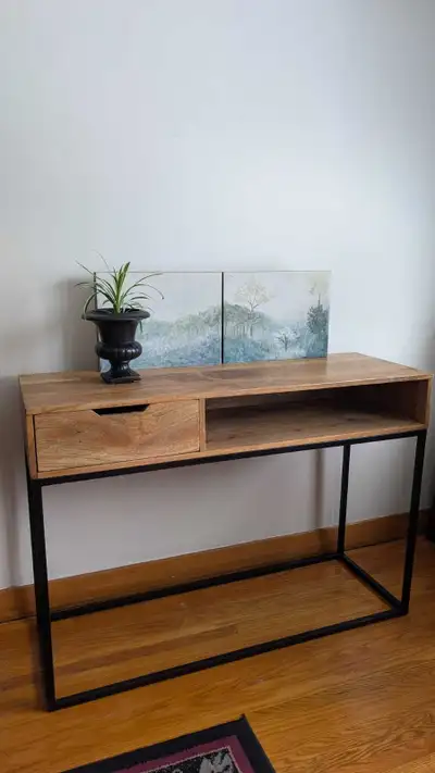 This console table features a stylish wood top with a sleek black metal frame, and includes a drawer...