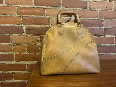 A vintage Ebonite bowling ball bag in tan with metal ball bar rack and "Joy" engraved on the zipper....