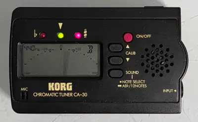 Black chromatic tuner. Displays the note and tuning. Features mic and input. Has buttons for on/off,...