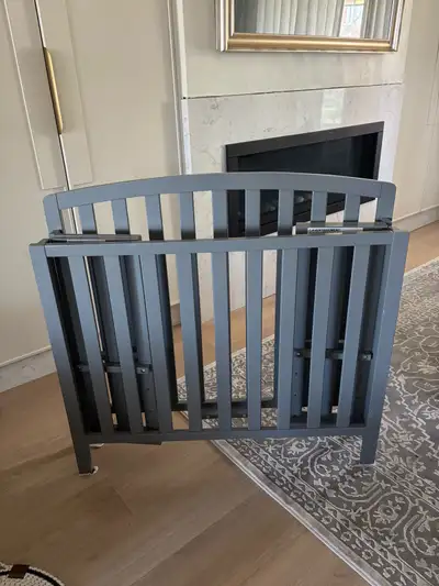 Grey Wooden mini fold up Crib. Easy to use in a smaller space or as an extra crib at a grandparents...