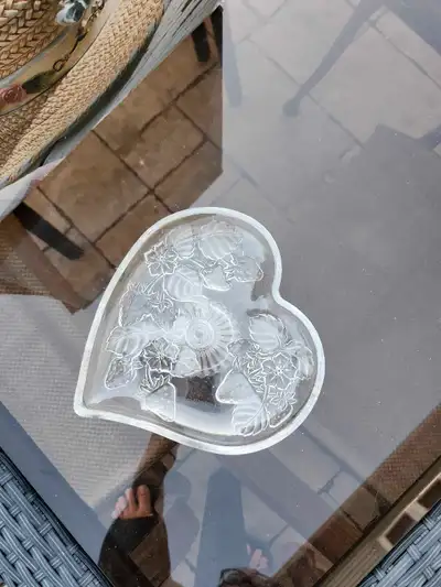 A glass pedestal dish in the shape of a heart with an etched design of strawberries and leaves. It i...