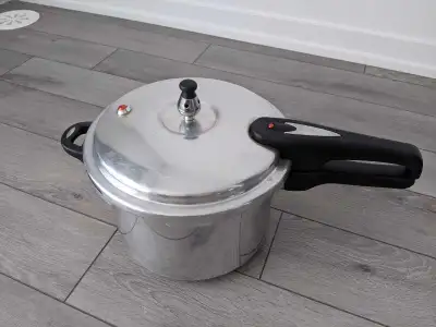 Stainless steel pressure cooker with black handles. Includes a pressure release valve and safety ind...