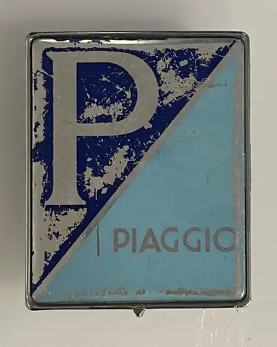 This is a used Piaggio emblem. It would be great for restoration on a vintage scooter. A bit of wear...