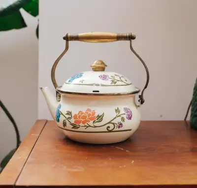 A cheerful little enamel kettle with bright blue, coral, and lavender florals, brass-tone handle, an...