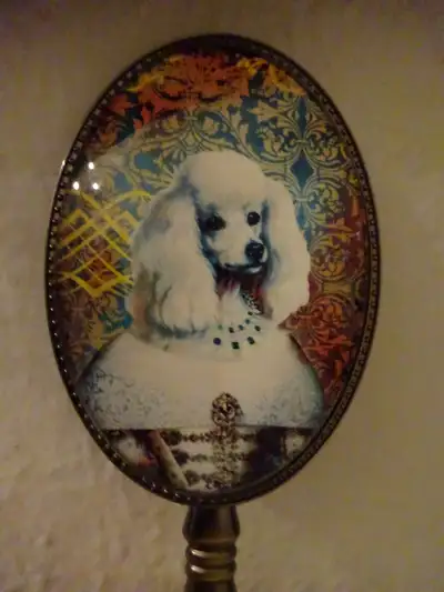 miroir royal ovale a manche en étain avec d une caniche habillée en reine. ce miroir proviens d Ital...