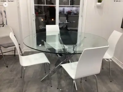 This modern dining table features a sleek glass top and a unique, star-shaped chrome base, perfect f...