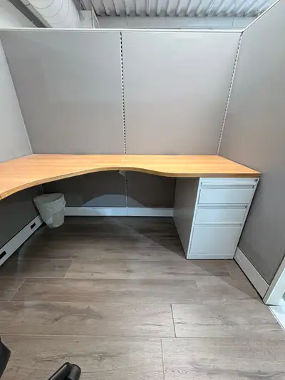 Spacious L-shaped office workstation has a wood-grain laminate desktop and grey fabric privacy panel...