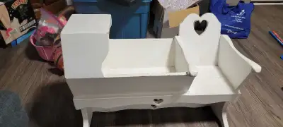 This charming white wooden doll cradle features a classic heart cut-out design and is perfect for im...