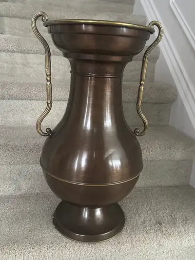 This decorative vase features a classic urn shape with ornate handles. It's crafted from metal with...