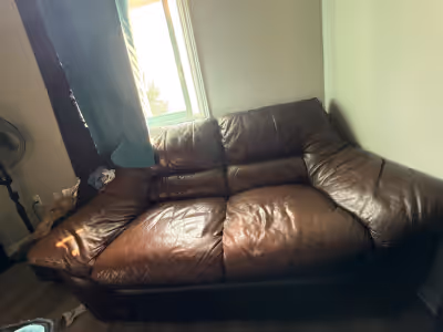 This is a brown leather two-seater couch, perfect for a cozy living space, with dimensions of approx...