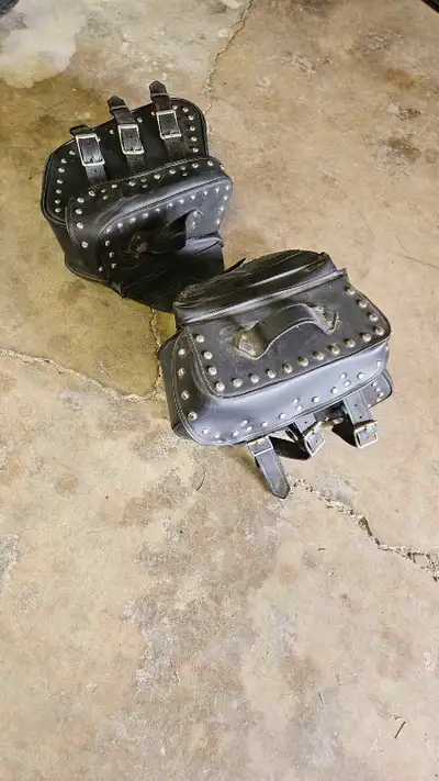 These are a pair of used black motorcycle saddlebags, adorned with silver studs and buckle details,...