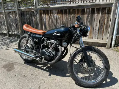 This custom cafe racer 1974 Honda CB360 features a sleek black frame, a stylish brown quilted leathe...