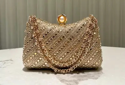 Shine bright with this dazzling gold, jeweled clutch featuring a delicate chain strap, perfect for a...