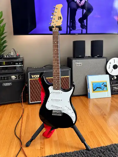 AXL electric guitar in a classic Strat-style design with black finish and white pickguard. Has 3 sin...