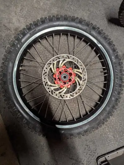 This is a dirt bike wheel with tire and brake disc, perfect for off-road adventures. It's in good co...