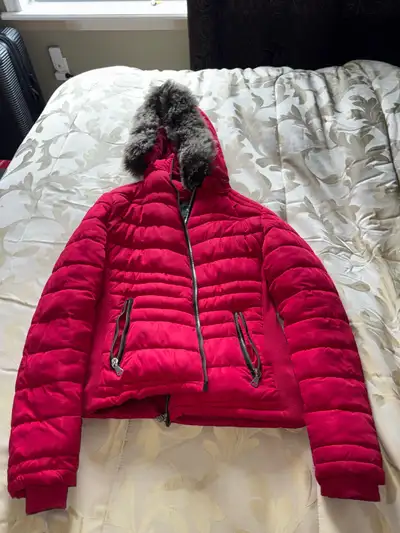 Red quilted puffer jacket. Features a faux fur lined hood and zipper closure. Two zippered pockets....