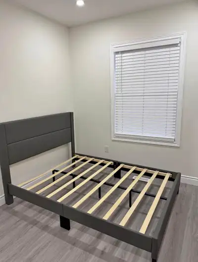 This queen-sized bed frame features a modern design with a grey upholstered headboard, providing bot...