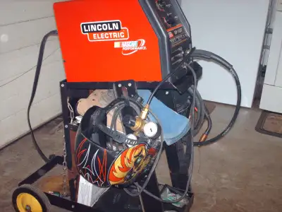 SP-135T Lincoln MIG Welder and cart, face masks, welding apron, box of welding wire, etc.