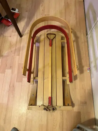 Classic wooden sled with red accents and a pull rope. It's made of durable wood and ready for winter...