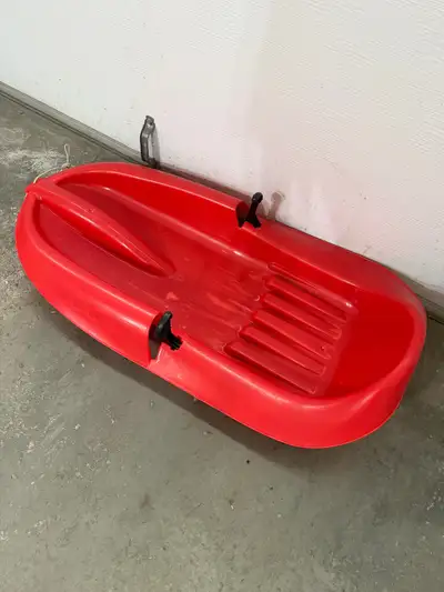 Small red plastic sled with brakes. Has a short tow rope to pull little ones when they get tired!