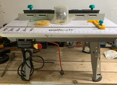 This pre-owned Wolfcraft router table paired with a Rockwell 6702C router offers a sturdy and versat...
