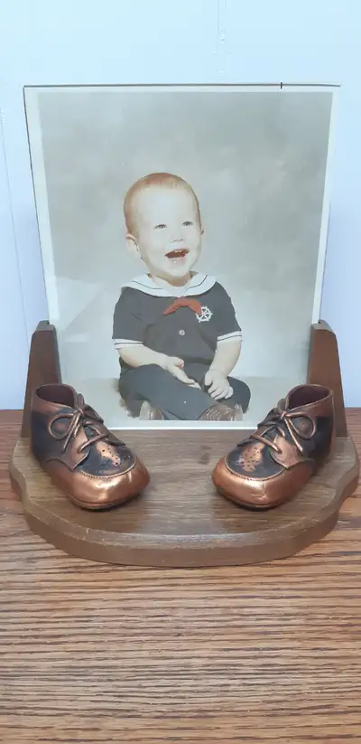 Vintage (70’s) bronzed pair of baby shoes on wooden base with 8”X10” glassed frame behind. Photo not...