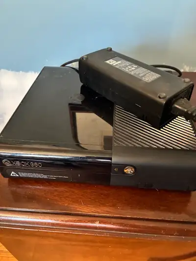 Black Microsoft Xbox 360 E console with original power supply brick and power cable. This unit has a...
