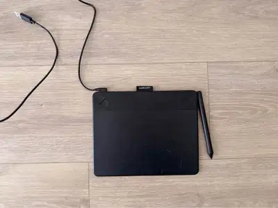 Black Wacom drawing tablet. It has a stylus and a USB cable.