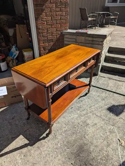 This elegant, pre-owned vintage console table features convenient drop-leaf sides and three storage...