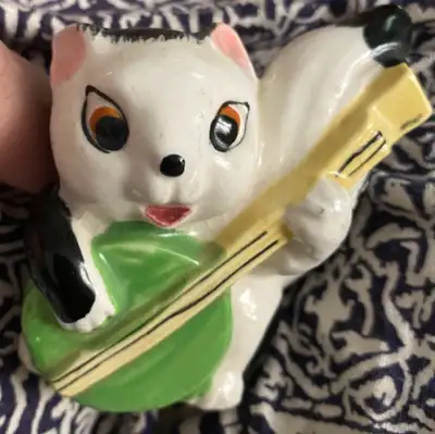 Small ceramic skunk figurine from the 1950's. The skunk is about 3.5 inches tall and is holding a ba...