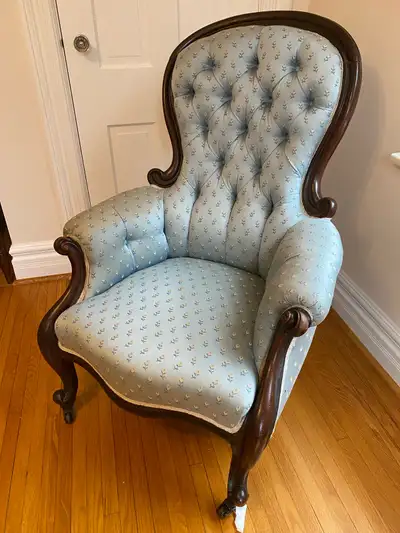 This Victorian gentleman style chair, with its ornate dark wood frame and light blue patterned fabri...