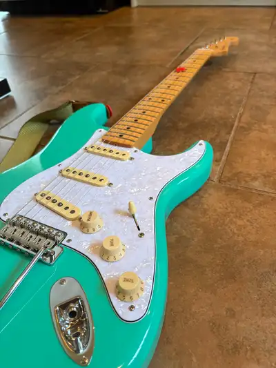 This Fender Stratocaster electric guitar features a classic seafoam green finish, a signature maple...