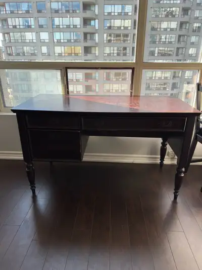 A classic dark wood writing desk with three drawers. The top surface has some wear, and the front dr...